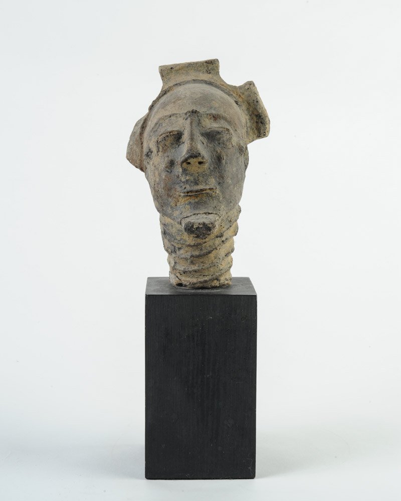 Anyi Agni Terracotta Memorial Head: Portrait head with closed, coffee bean eyes, delightful half-smile, ringed neck, facial scarification, striking headdress. Appears to have significant age. Mottled dark grey surface. Repairs to beard 