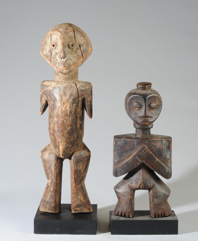 Two Lega Figures, D. R. Congo: The largest a Bwami Society Inginga type figure with arresting, hollow eyes in a heart shaped face over a simplified, almost Cubist, body. Tiny fragments of mica or ground shells or glass are fixed wi