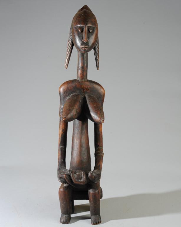 Bambara Maternity Figure: Carved wood figure with peaceful downcast eyes, bracelets on her upper arms, a sleeping infant in her lap. Bambara people, Mali, West Africa. Approx. 25" in height. Provenance: Estate of Thomas McNema
