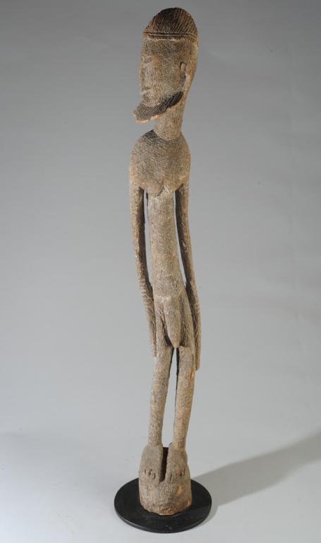 Standing Dogon Male Figure: Curved standing bearded figure looking to his right. Textured surface with allover impressed marks. Breaks to beard. On custom gallery stand. Approx. 45 1/2" H.Provenance: Estate of Thomas McNemar, (1