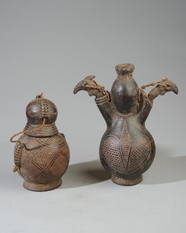 2 Bamum Spirit Pots Terracotta Vessels: One round pot with incised geometric decorations, the cover attached by a twisted fiber rope. The larger pot with one central opening and two side spouts, the spouts with stoppers in the form of the h