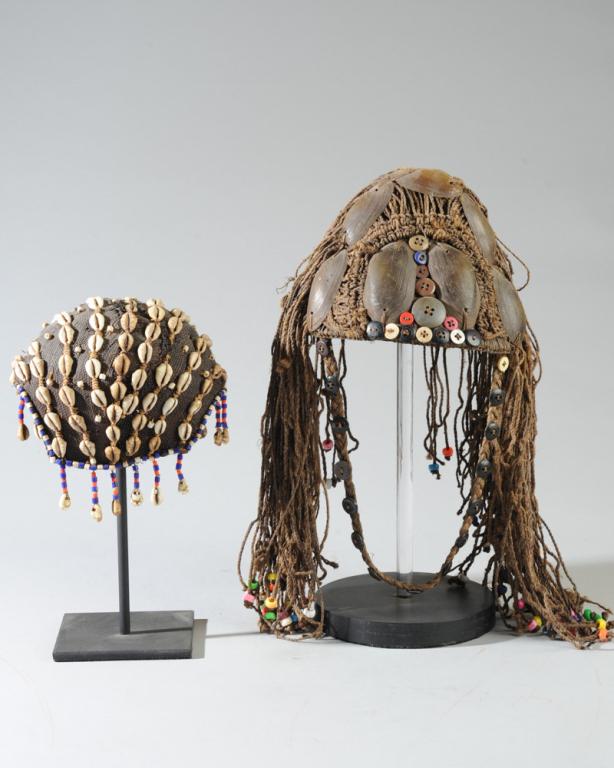 Two Lega Hats: Embellished with buttons, fiber, shells. Each on gallery stand. Lega people, Congo.Provenance: Estate of Thomas McNemar, (1931-2020.) McNemar lived and collected throughout Central and West Africa in 