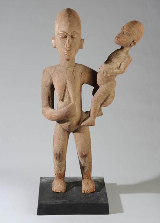 Lobi Maternity Figure: Tender Lobi wood carving of a mother carrying her child against her hip. On gallery stand. Burkina Faso. Sculpture approx. 29 1/2" in height. With stand approx. 32".Provenance: Estate of Thomas McNema