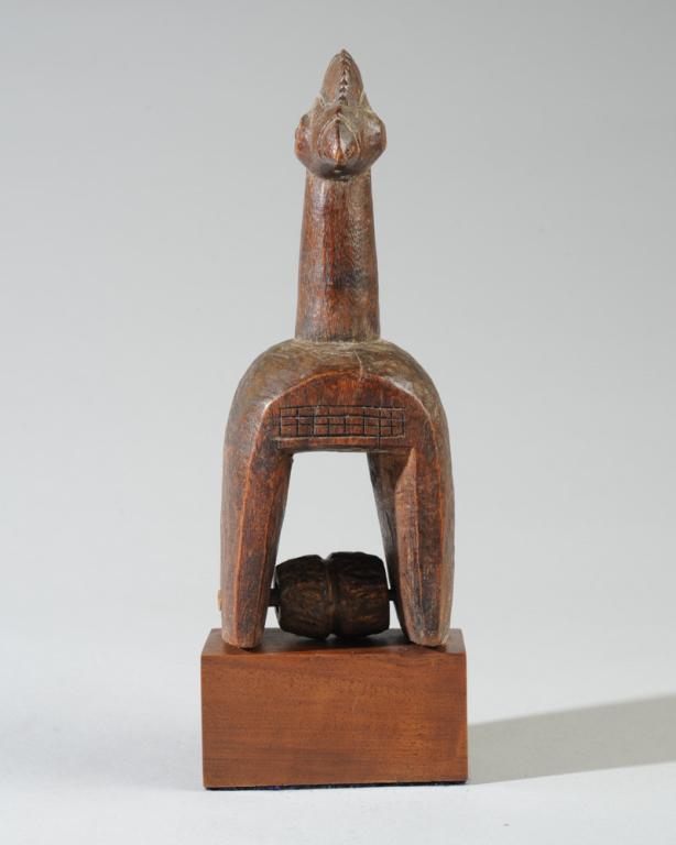 African Janiform Heddle Pulley: Carved wooden heddle pulley with two crested cockerel heads facing opposite directions on a long neck. On custom gallery stand. Pulley, approx. 7" x 2 3/4" x 2 1/4". Provenance: Estate of Thomas McNem