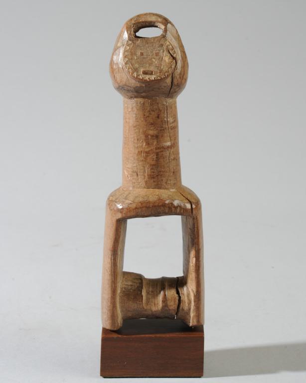 Baule Heddle Pulley: With Goli mask finial on long thick neck. Spool section integral and fixe; not cut away. Crack to spool, splits. On custom gallery base. Pulley approx. 7 1/2" H. Provenance: Estate of Thomas McNemar,