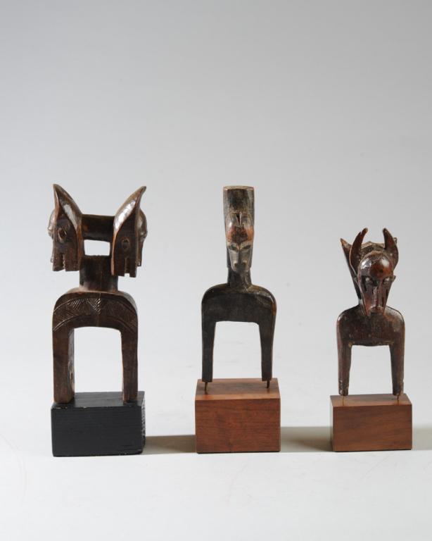 Three Janus Head African Heddle Pulleys: The largest with opposing Bo Nun Amuin mask heads over incised body. The smallest with two different zoomorphic heads. The third pulley with a central post supporting two heads with curved, ram-like h
