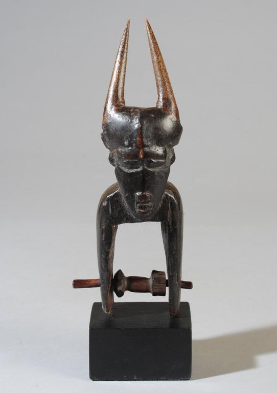 Senufo Djimini Heddle Pulley: Anthro-zoomorphic pulley with horned, mask like face on curved neck. The long pointed horns were either carved separately, or are repaired/ replaced. Ivory Coast. On custom gallery stand. Pulley, appr