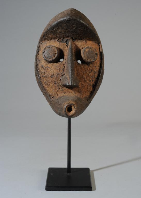 Grebo Mask: With steep overhanging forehead, protruding disc eyes, large nose and cone-shaped, tubular mouth. Black and reddish brown heavily encrusted surface. Grebo people, probably Liberia. On custom gallery s