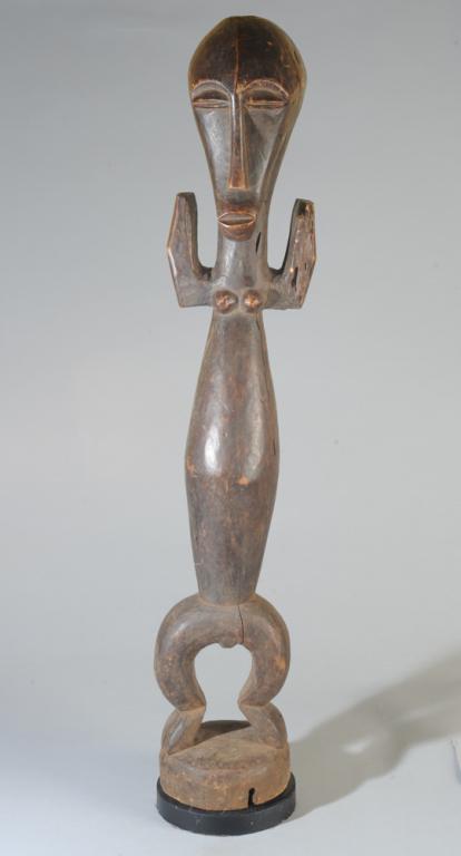 Lega Figure, D. R. Congo: Standing figure, the long, mask-like face with arched brows, coffee bean eyes, long slender nose and out-thrust lips. The long-waisted body with truncated arms held up, small high breasts, short, bowe