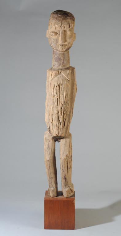 Dogon Standing Figure: Face with simplified features, coffee bean eyes, small pouting mouth, thick neck, arms carved close to the cylindrical torso, legs slightly bent. On Custom gallery stand. Figure approx. 31" H, with st