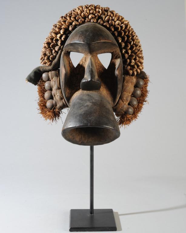 We / Guere Mask with Accoutrements: Abstract anthropomorphic mask with jutting brow, triangular eye holes, cheeks and nose, and with a large megaphone-shaped mouth. With headdress of shells, metal bells, raffia, and hand-woven fabric. L