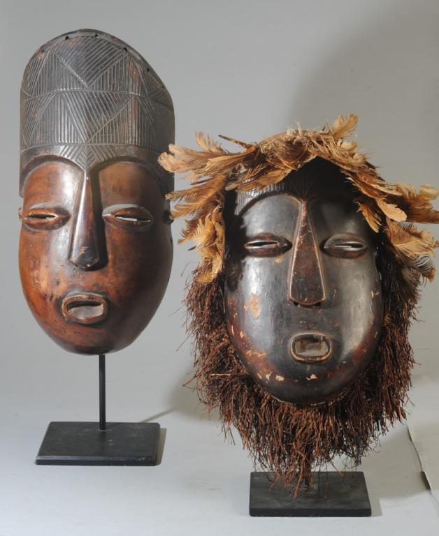 Zande Male & Female Masks: Mask pair, both with crown-like coiffures above full, rounded faces, coffee bean eyes, long triangular noses and protruding lips, the male with a higher hairdo. The female retains her feathered headdr