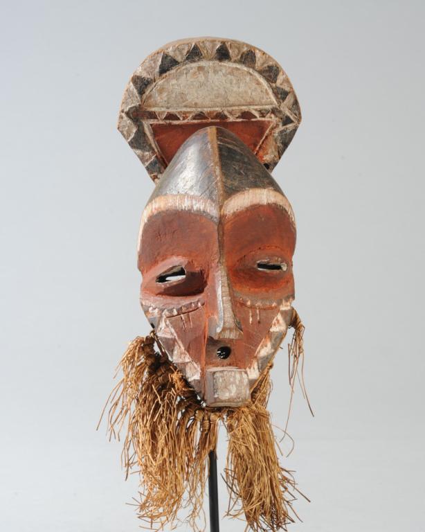 Miniature Pende Mask: The plate-like headdress rises behind the steeply projecting forehead over half-closed coffee bean eyes, sharp nose, small round mouth orifice and square projecting chin or beard. Raffia collar. Black