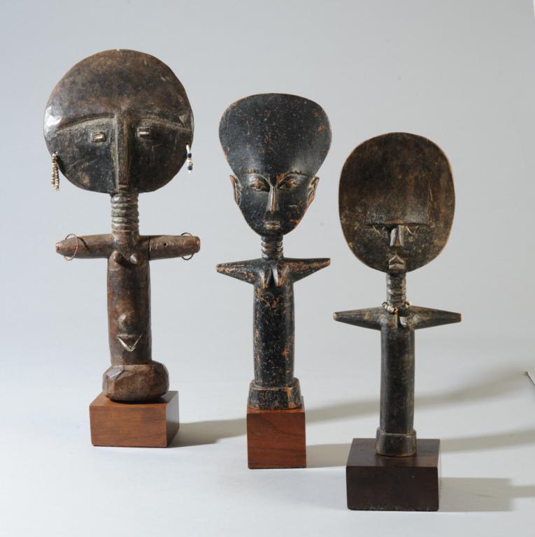 Three Ashanti Akuaba Fertility Dolls: One with unusually detailed and naturalistic facial features, including ears, the remaining two with traditional minimalist features and round heads, all with cylindrical bodies, small breasts, round 