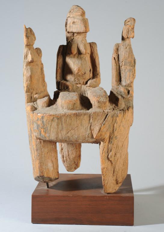 West African Shrine Figure: Possibly a Nigerian Ikenga shrine figure. Three female figures with crested coiffures kneeling atop a footed platform. Very weathered. Likely a shrine object. On custom gallery base. Dimensions of car