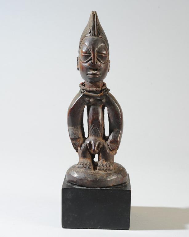 Yoruba Ibeji Male Twin Figure: Small carved wood figure with high coiffure, large bulging closed eyes, long torso with arms at sides and short legs, feet on carved round base. Neck encircled with small old trade beads. On custom ga