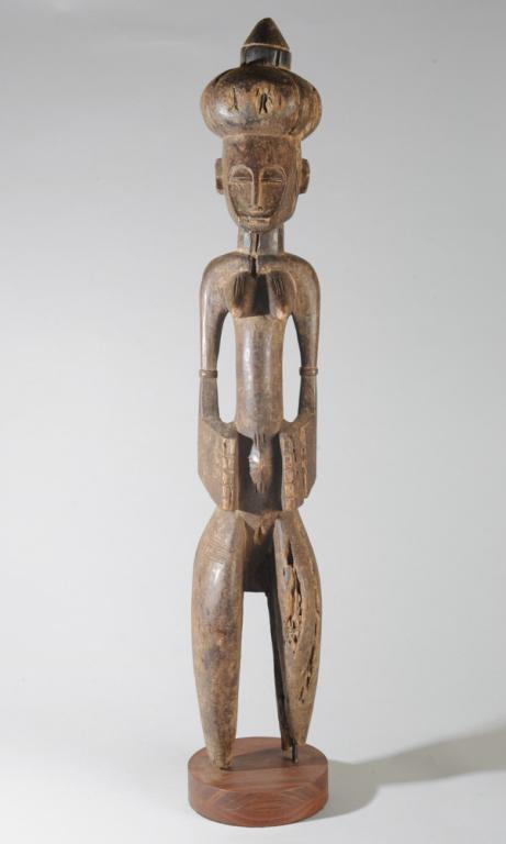 Senufo Standing Female Figure: Finely carved figure with unusual coiffure, headdress, or bundle carried on the head, the heart shaped facial plane with large half closed eyes, long slender nose, steeply angled jaw. The body with pr