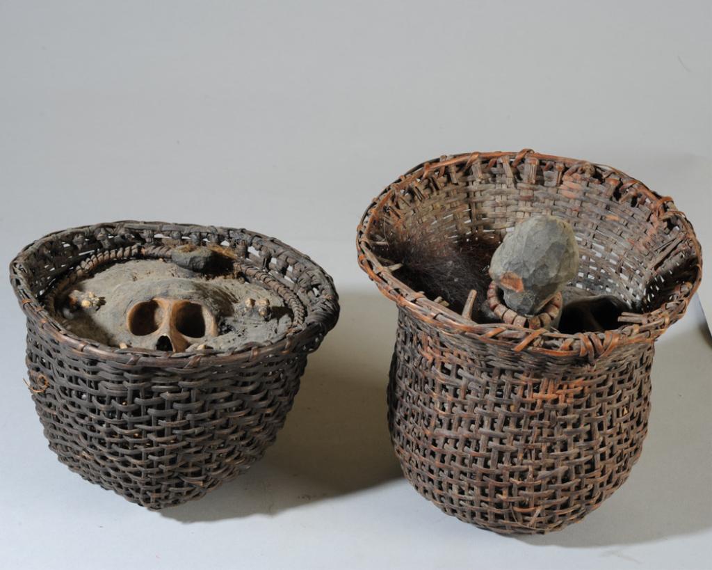 Two African Fetish / Power Baskets: Possibly Bulu people, Cameroon. One basket with monkey skull, teeth, and other objects embedded in organic material. The other basket with monkey skull, carved and pigmented wooden female figure, bead