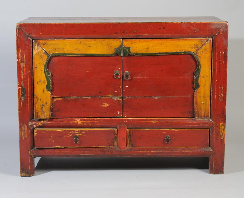 Red Lacquer Mongolian Chest: With two doors (left door disconected) opening to a shelf, over two drawers on four low feet, and with yellow and green lacquer trim. In as-found condition.Approx. 42" L x 16"W x 31" H.