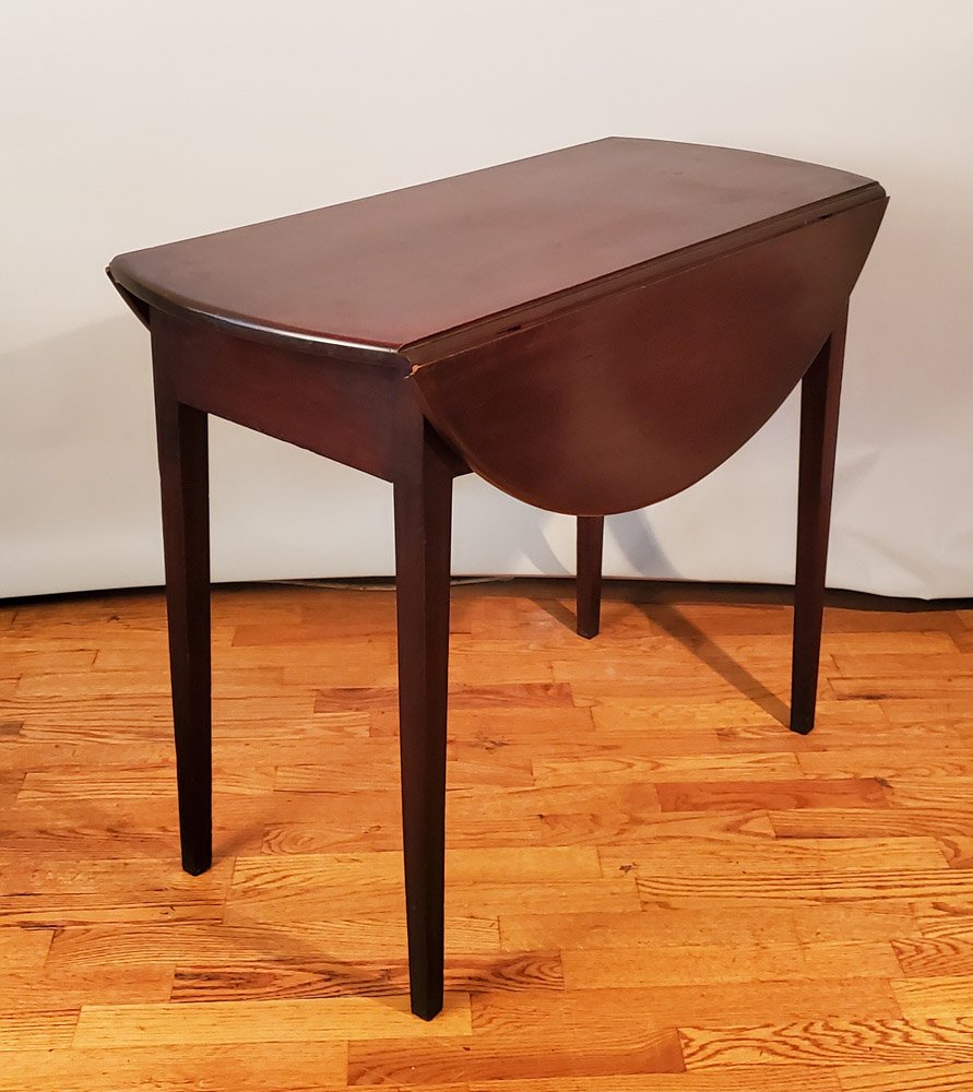 Diminutive Hepplewhite-style Pembroke Table: Two-board top with two, one-board leaves which, when raised, create a circular surface, above a pinned, mortised and tenoned case, the whole supported on square tapered legs. Mahogany with unidentifie