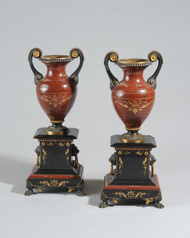 Pair of Gilt and Marble Garniture Urns: Pair of gilt decorated red marble garniture urns, on plinths with lion's head motif, one with chip to backside under urn, in as-found condition.H: approx. 12".