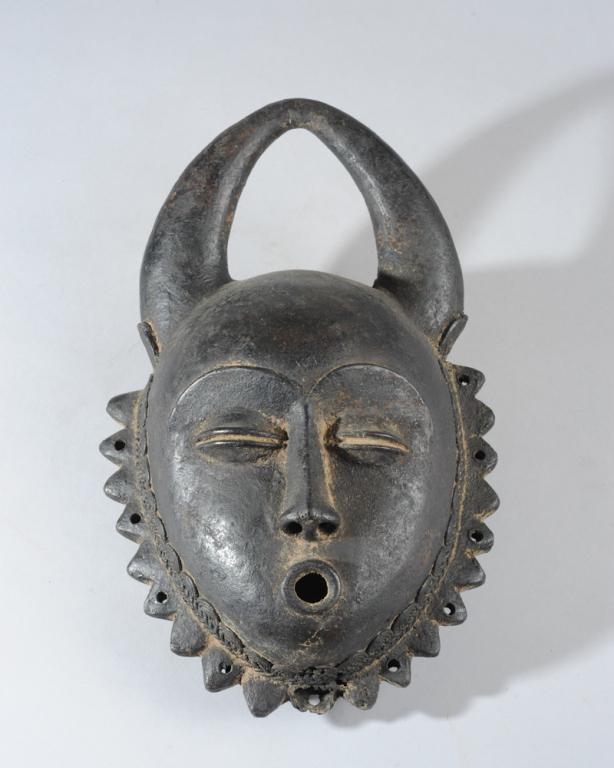 Bronze Yaure Mask, Ivory Coast: Bronze mask with rounded, curving horns joined at the tips above a heart shaped face with delicate features. The thin, arched brows over coffee bean eyes with slender nose and "o" shaped lips. The fac
