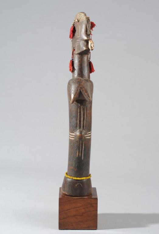 Mossi "Biga" Fertility Doll: With narrow, crested head, embellished with leather, string tassels, beads and shells. Women who hope to become pregnant wear such dolls wrapped within their garments. Mossi people, Burkina Faso. On c