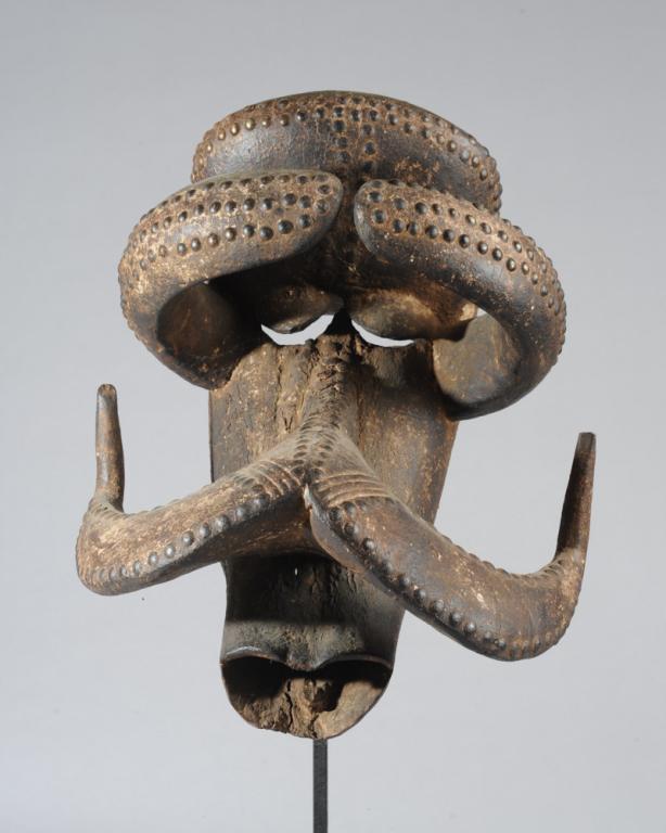 Bete Gre Mask, Ivory Coast: Fearsome mask of the type originally used to prepare Bete warriors for battle, with heavy, overhanging brow, and forward-curving projections over the downcast eyes above backward sweeping forms like t