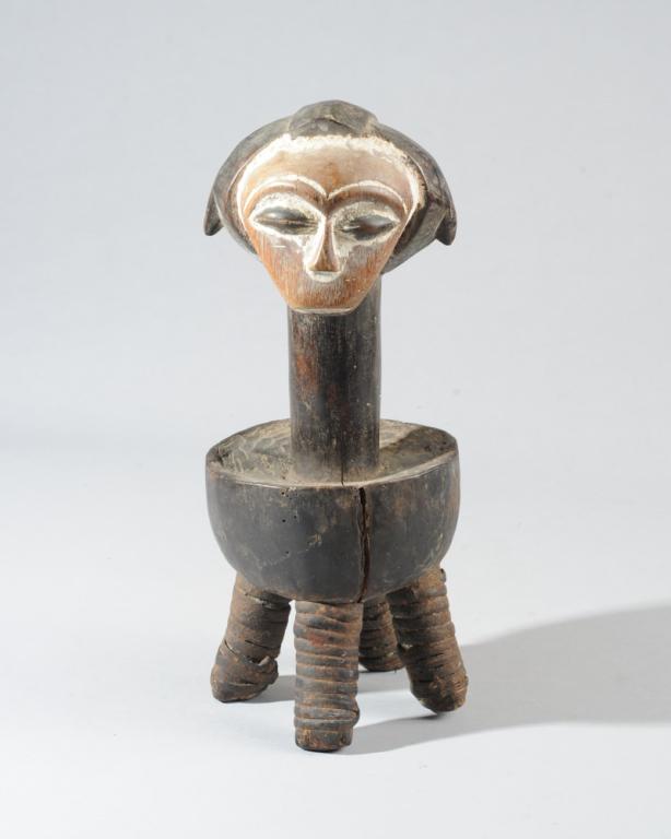 Kwele Altar, Gabon: Small four-legged stool surmounted by ancestral figure with complex, tri part coiffure, the heart shaped face with arched brows and closed coffee bean eyes highlighted with kaolin. The top of the stoo