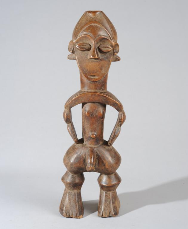 Fine Zande Male Figure: Well carved standing male figure, with flattened, heart shaped facial plane beneath rounded brow and carefully sectioned coiffure. The heavily stylized body with its balanced angles and curves, masses
