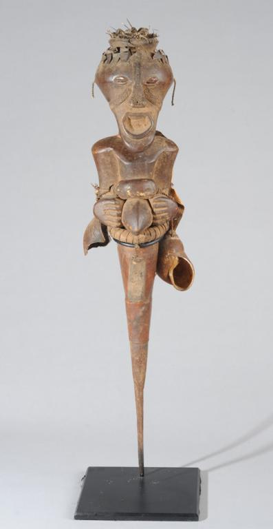 Songye Power Figure, D. R. Congo: Power figure or Nkisi with characteristic tapering head and positioned with arms at sides and hands cupping protruding umbilicus. Below the waist the figure descends in the form of a long sharp horn, 