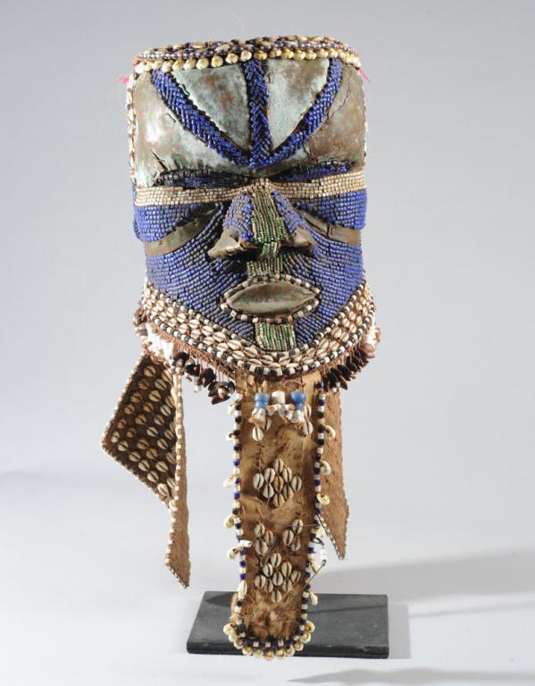 Kuba Bwoom Mask, D. R. Congo: Helmet mask with sheet copper, beads, shells, seed pods, fabric and animal hide. Such masks are used in dances which tell of the founding of the Kuba kingdom. On custom gallery stand. Mask approx. 9" 