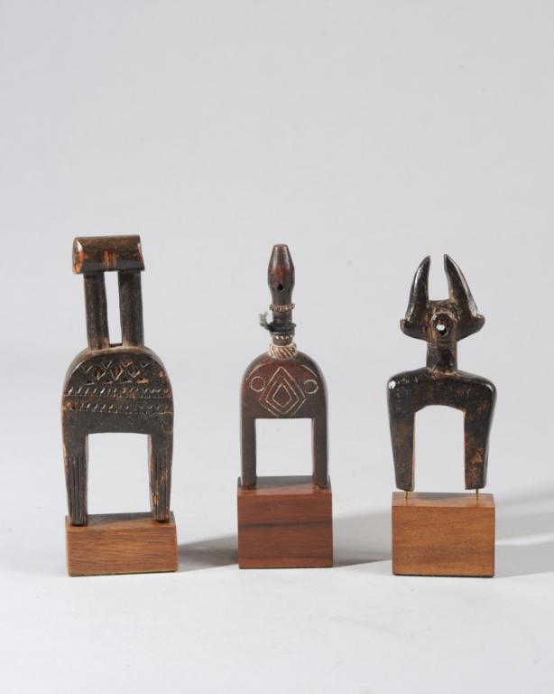 Three African Heddle Pulleys: All of abstract form, one suggesting a horned creature, the largest with chip carved surface. All on custom gallery stands. Tallest (including stand) approx. 7 1/8" H. Provenance: Estate of Thomas McN