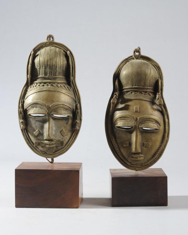 Pair African Bronze Masks: Small male and female bronze masks made with the lost wax technique, both with elaborate high coiffures and elegant facial features, the male distinguished by a neat beard. Two finely formed grasshopp