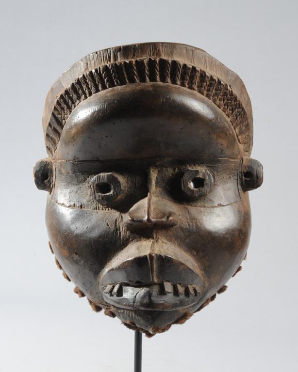 Dan Guere / Wee Mask: Anthropomorphic mask with plaited hair above steep forehead, with tubular eyes, round cheeks, and teeth poking out between full lips. The chin is bearded with small round tufts of animal hair. Wee / G