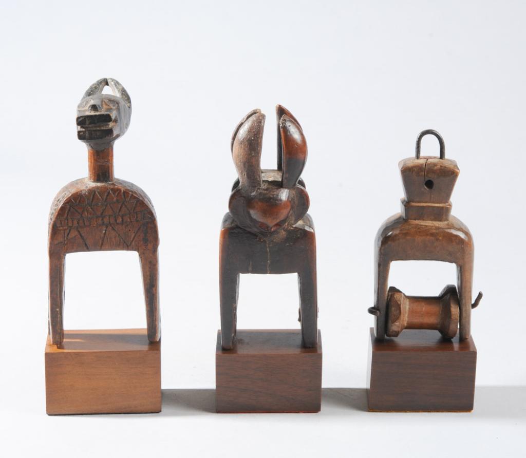 Three West African Heddle Pulleys: To include one Baule Bo Nun Anuin pulley, a janiform horned figural pulley, and a pulley with abstract geometric finial. All on custom gallery stands. Tallest, including stand, approx. 7 3/4" H. Prove
