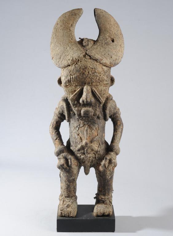 Ligbi Masked Figure, Ivory Coast: Male figure wearing typical horned mask with downcast eyes and side projections. The figure stands firmly on strong legs, knees slightly bent, hands on thighs. Six leaf-shaped scarification marks radi