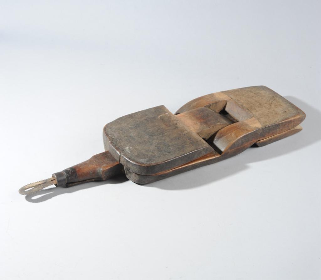 Zaramo Seat Coconut Grater, Tanzania: Folding low stool with metal sawtooth projection on one end for grating coconut while seated. Surface of the seat with chip carved patterns and smooth, well worn surface. Approx. 22 1/2" L. Provenance