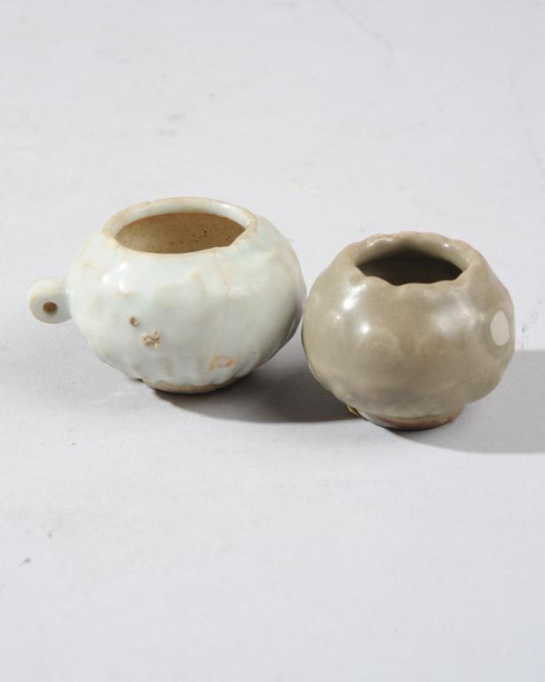 Two Ming Celadon Bird Feeders: The larger an early Ming bird feeder with pale Ching-pai glaze over raised scrolling at lip, fluting at base. Tiny 'ear' handle. Several old thin stable hairlines, one tiny chip at rim. The smaller of