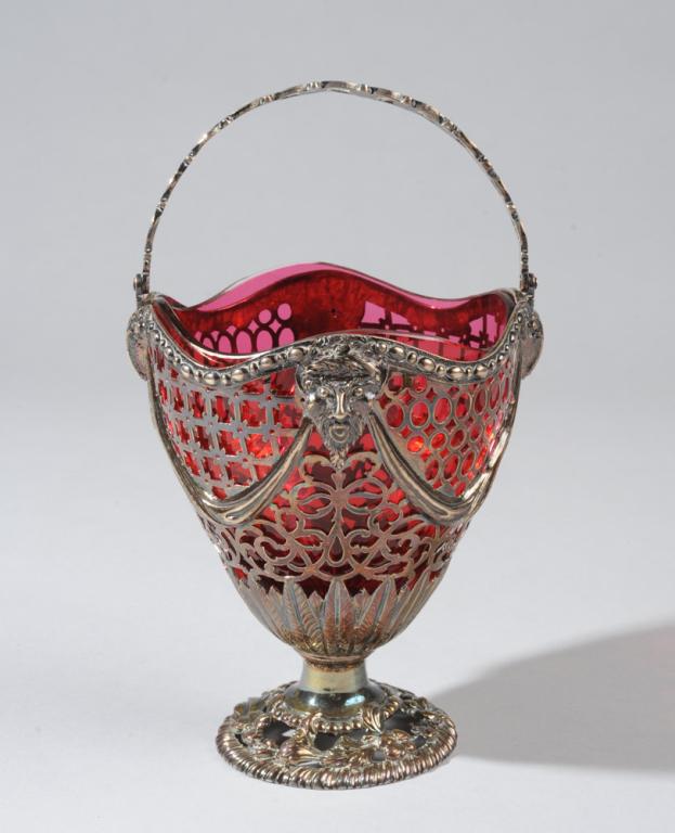Georgian Silver Sugar Basket w/ Ruby Glass: Reticulated English sterling silver basket with ruby glass liner. Repousse rams heads and laurel crowned satyrs with plain and beaded swags on square and arabesque openwork above palmettos arising fro