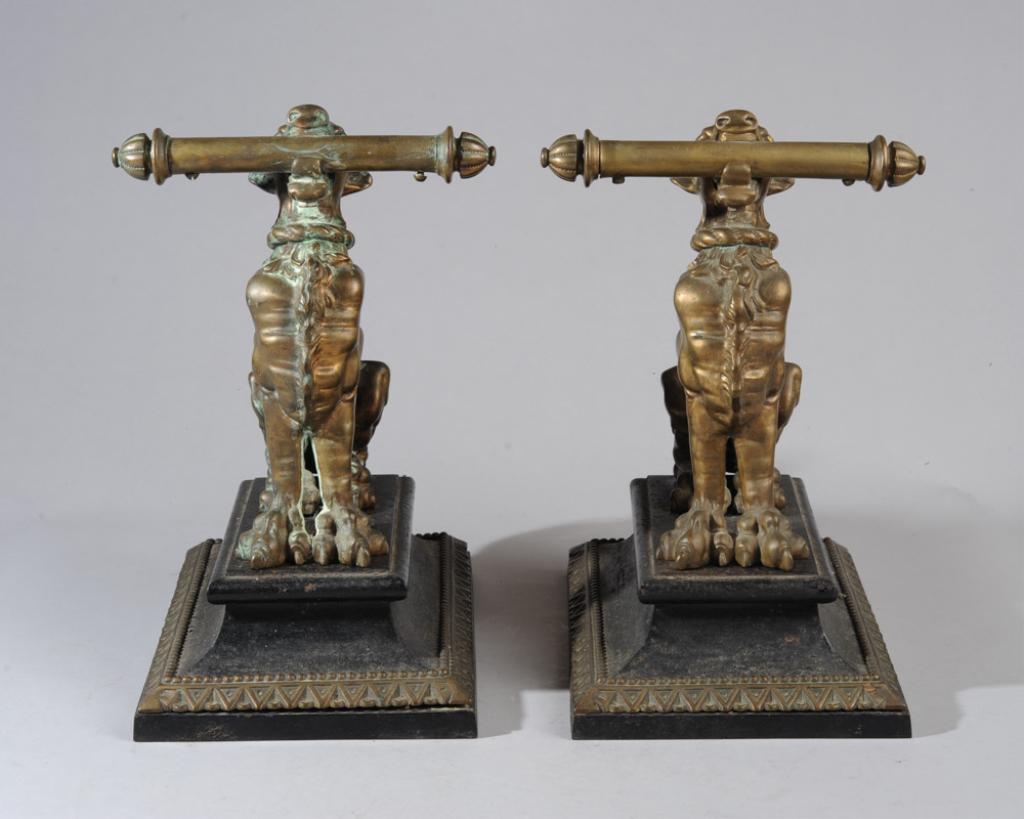 Large Bronze Foo Dogs: Seated bronze foo dog andirons, the guardian animals grasping batons in their mouths, tails held high, on rectangular iron bases. Approx. 15 1/2" H. x 12 1/4" L x 8 1/4" W.