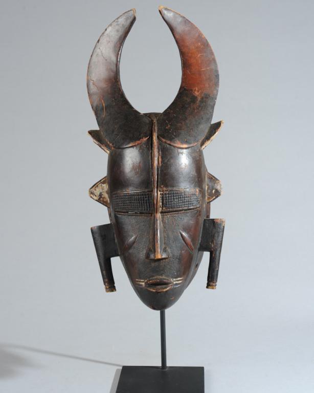 Ligbi Mask, Ivory Coast: Finely carved mask with flat, curving horns sweeping back from the forehead, the cranial ridge extending to the bridge of the nose, slit eyes beneath relief carved cross-hatched rectangular brows, the