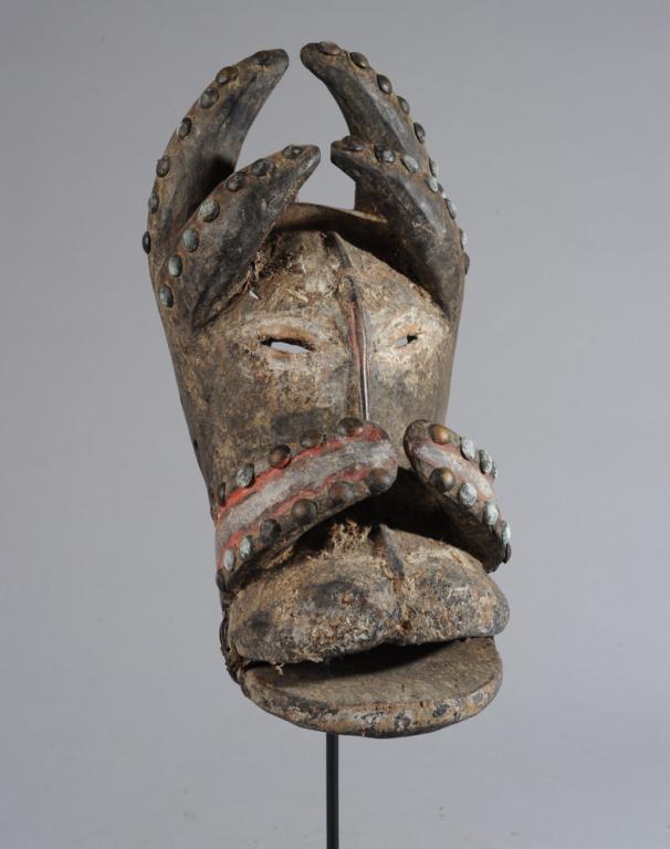 Bete Mask, Ivory Coast: Small mask with double horns on each side of brow and tusk-like projections on either side of snout, the encrusted surface embellished with lines of brass tacks. Includes custom gallery base. Mask, ap