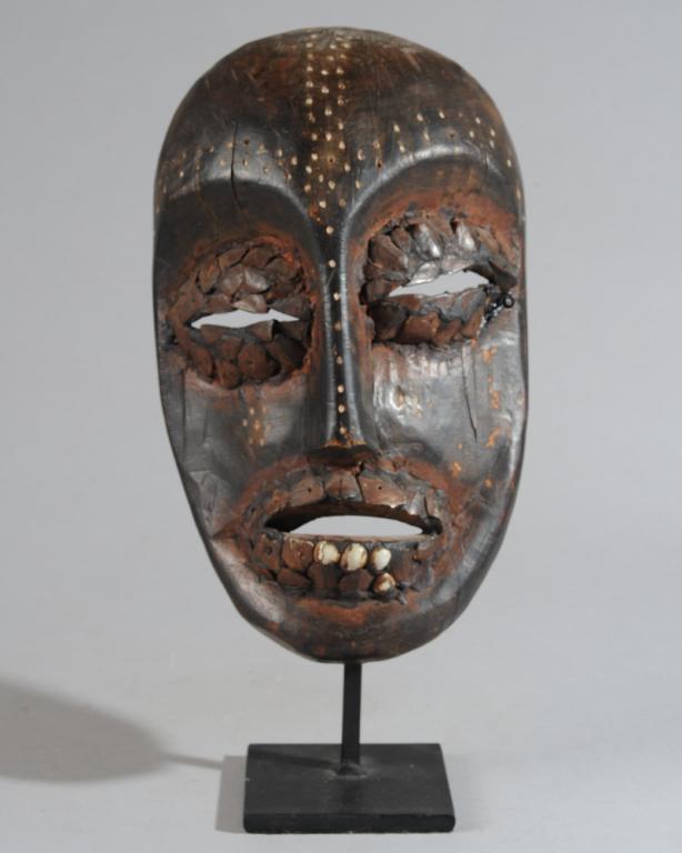 Lega Mask, Democratic Republic of Congo: Carved wood Bwami Society type mask with darkened fragments of seashells clustered around the eyes and mouth, and with lines of small holes filled with white kaolin patterning the forehead, nose, and 
