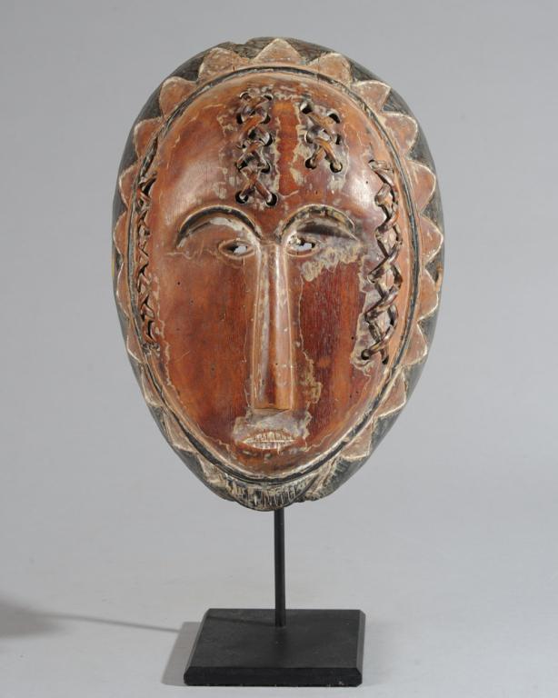 Fang Adouma Mask: Carved wooden mask with sawtooth pattern at rim, small eyes and mouth and long slender nose, short goatee. The surface of the face with holes supporting strips of cane laced in pattern of X's, decorat