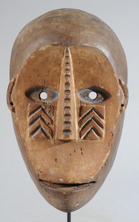 Ngbaka Mask, Zaire: Anthropomorphic mask with concave, heart shaped facial plane bisected by long, slender nose notched along its length, the almond shaped eyes with remnants of blue pigment in the whites. Below the eyes