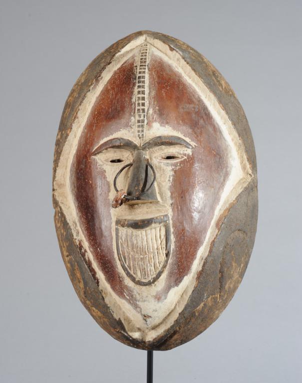 Ijo or Kete Mask: Large wooden mask, the face diamond shaped within a carved wooden cowl, with a relief carved checkered ridge from top of head to bridge of nose. Small eyes and large toothy smile. Kaolin and black pig