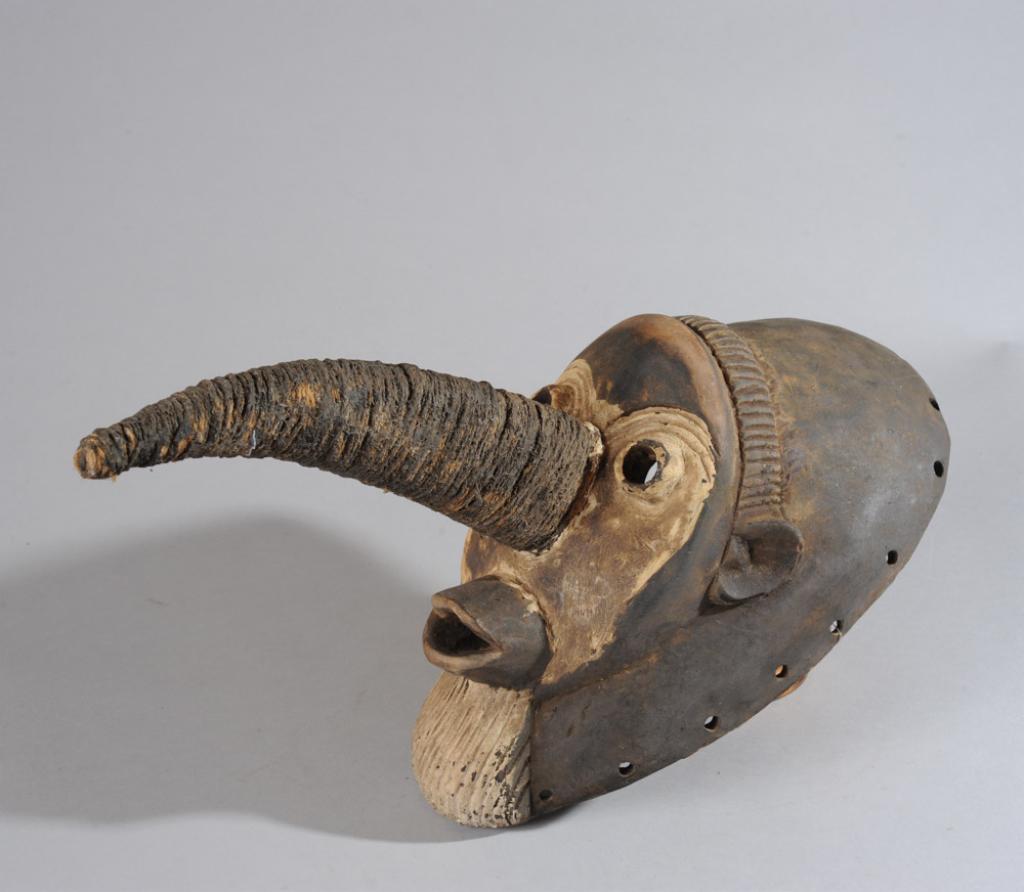 African Avian Mask: Carved wood bird-like mask, the long beak wrapped with fiber rope embedded with mud, and with round bulging eyes, the small round ears and protruding mouth suggesting a monkey. Tribe and country of or