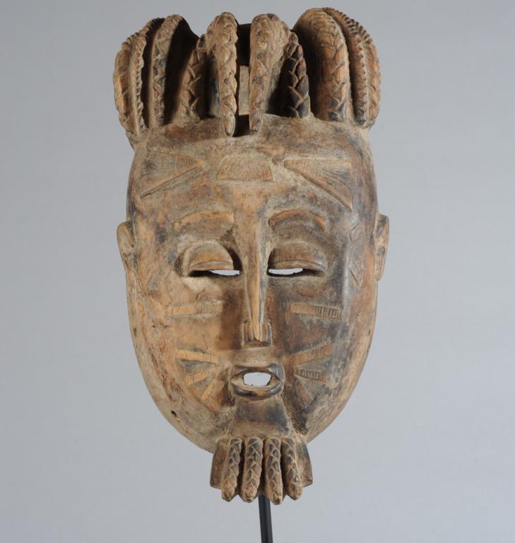 Baule Mask, Ivory Coast: Substantial anthropomorphic mask with elaborately arranged plaited coiffure, relief carved facial scarification, half closed coffee bean eyes, slender nose above pouting lips, with plaited goatee. Bel