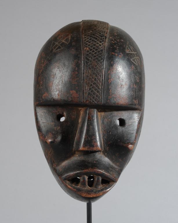 Kongo Mask: Anthropomorphic mask of blackened wood, with deep set eyes below a high round forehead, cross-hatched cranial ridge, sharp cheekbones, large mouth with prominent teeth, incised markings on forehead an